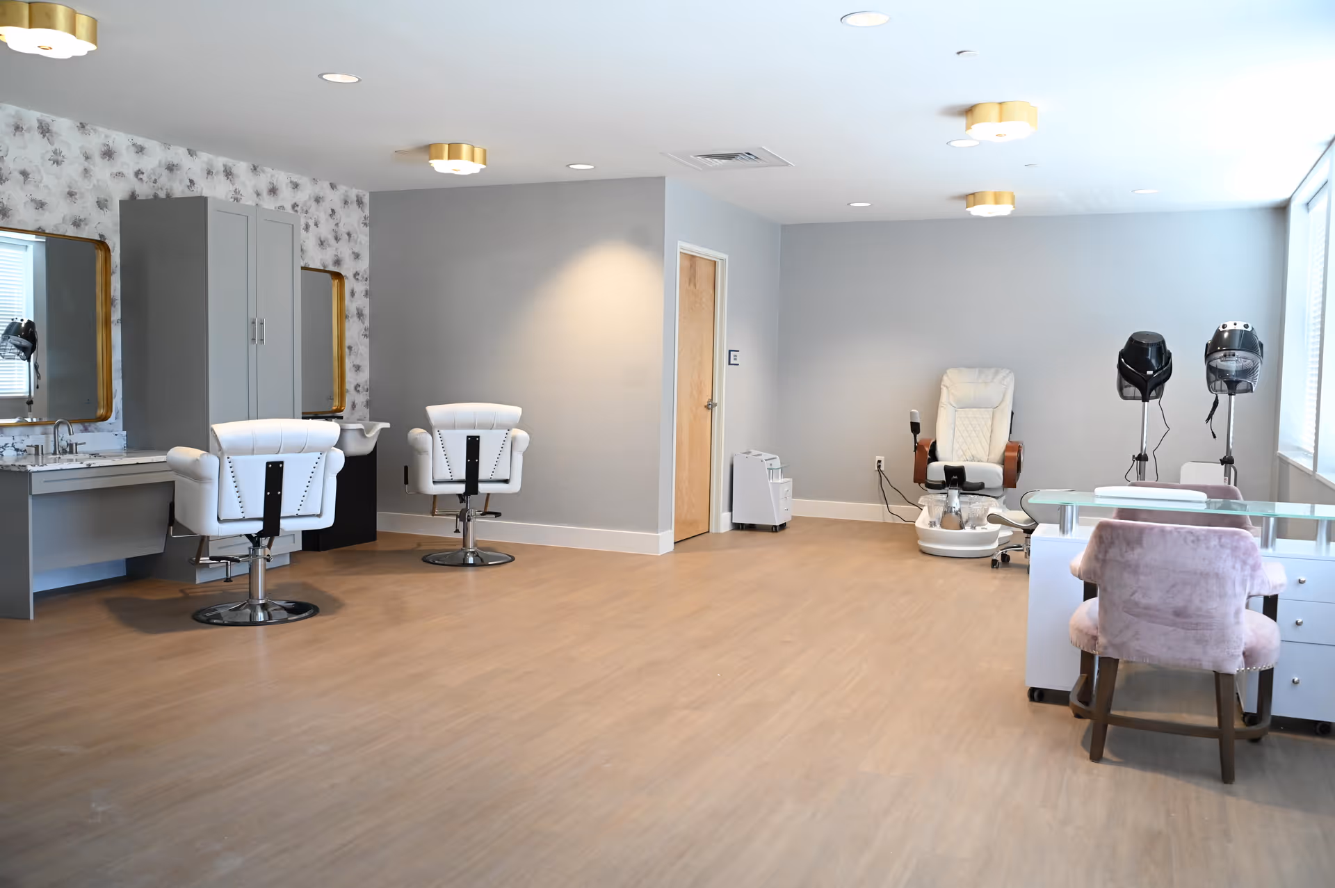 Spacious salon room with styling chairs, a pedicure chair, hair dryers and a manicure table in a senior living facility.