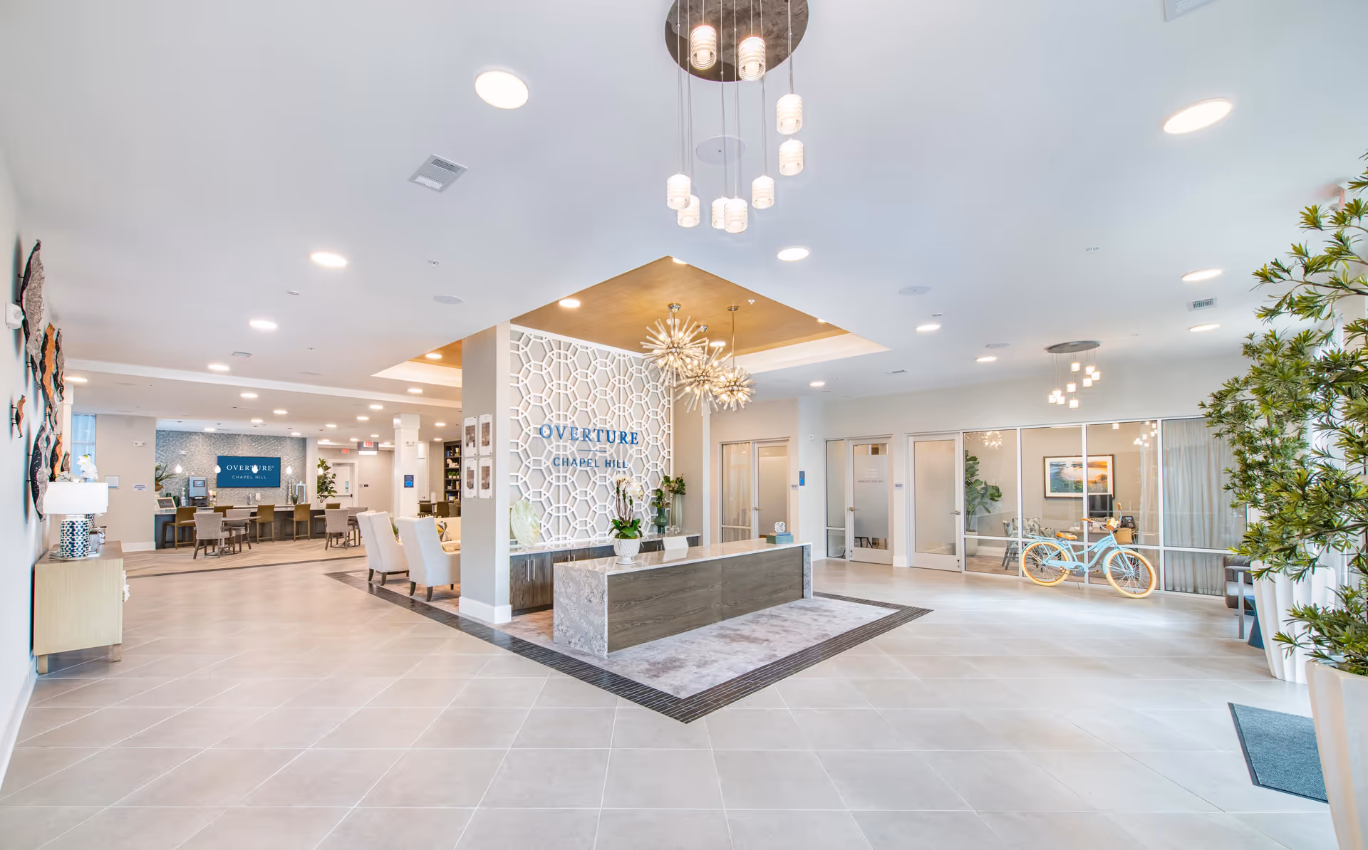 Bright, modern reception lobby of Overture Chapel Hill with a central front desk, seating areas, decorative partition, and plants.