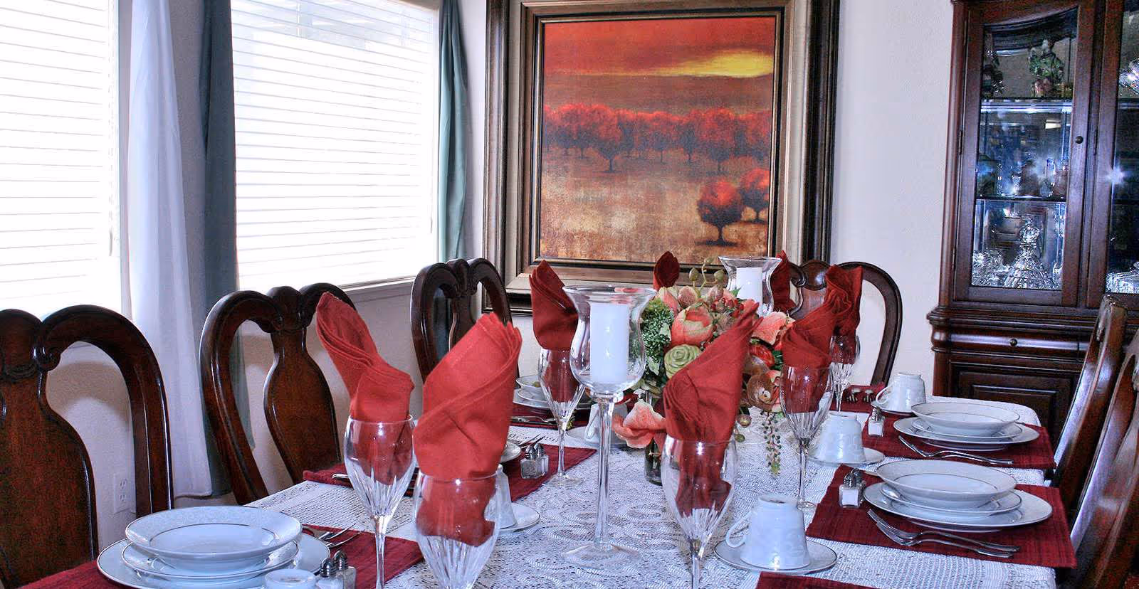 A formal dining room table set with plates, glasses, red folded napkins and a floral centerpiece.
