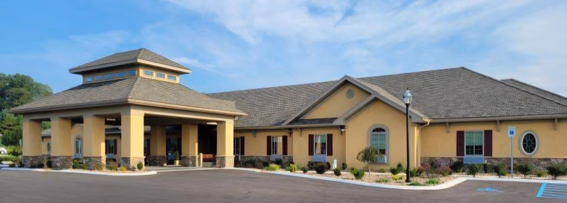 Single-story beige senior living facility with a covered entrance and landscaped parking area.