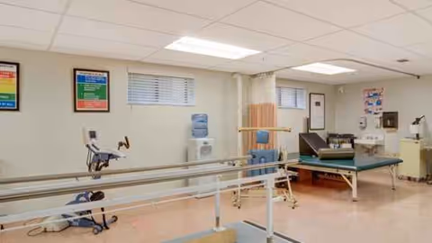 A rehabilitation therapy room featuring parallel bars, exercise equipment, and a treatment table.