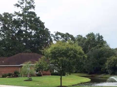 Well-maintained outdoor lawn with trees, a small pond, and a brick building.