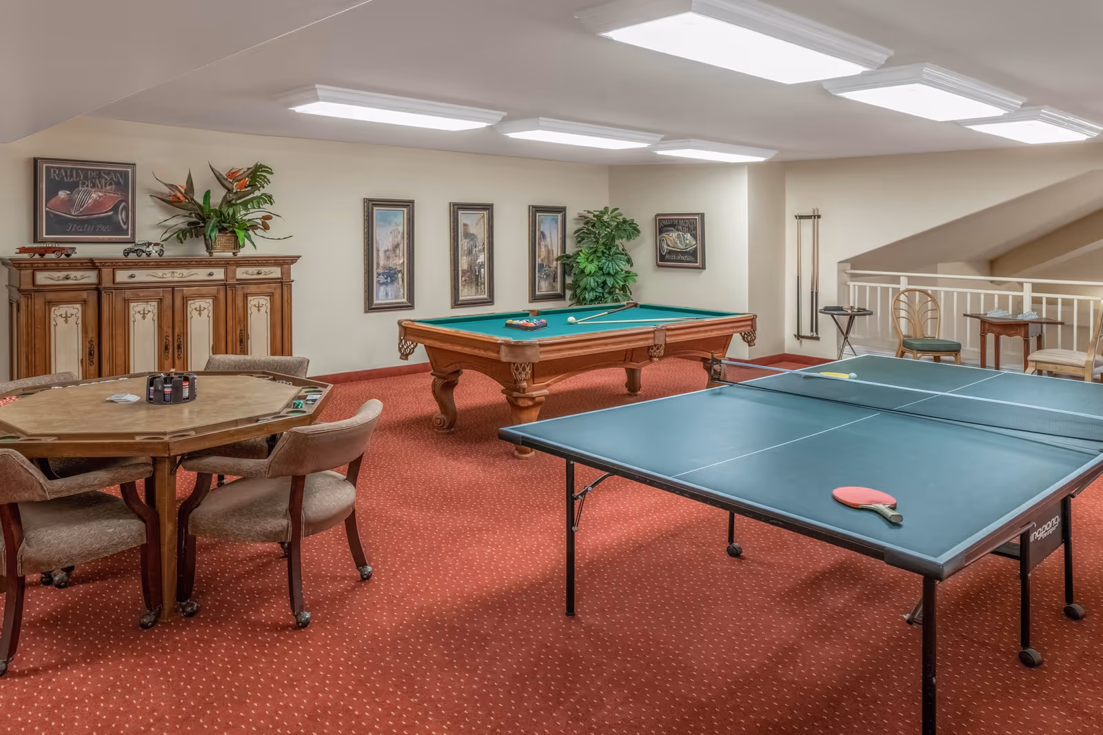 Recreation room with a ping-pong table, pool table and a card table with chairs on red carpet.