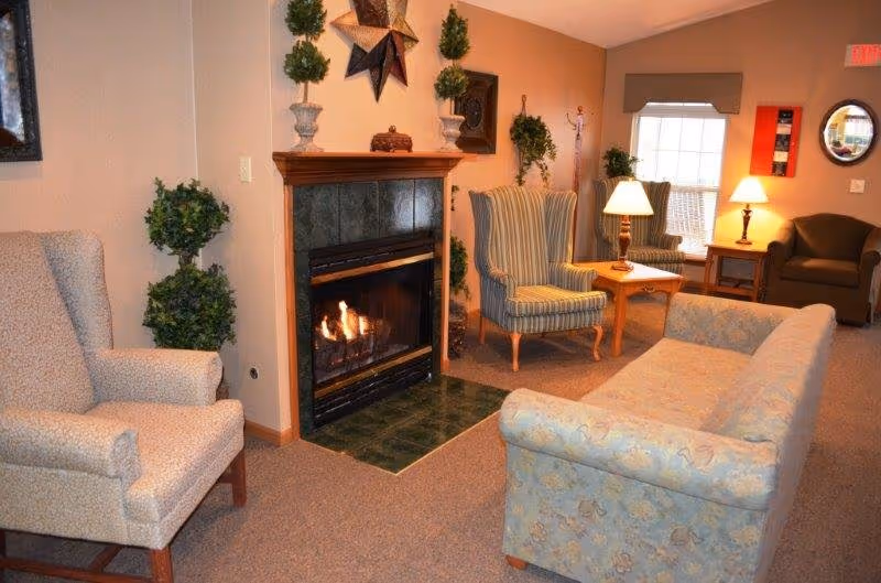 Cozy common room with a lit fireplace, armchairs, a sofa, side tables and lamps.