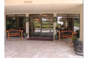 Covered building entrance with double glass doors flanked by benches, potted plants, and the number 5890 above.