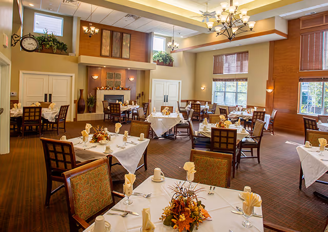 Bright, spacious dining room with multiple tables set with white linens, folded napkins, and floral centerpieces.