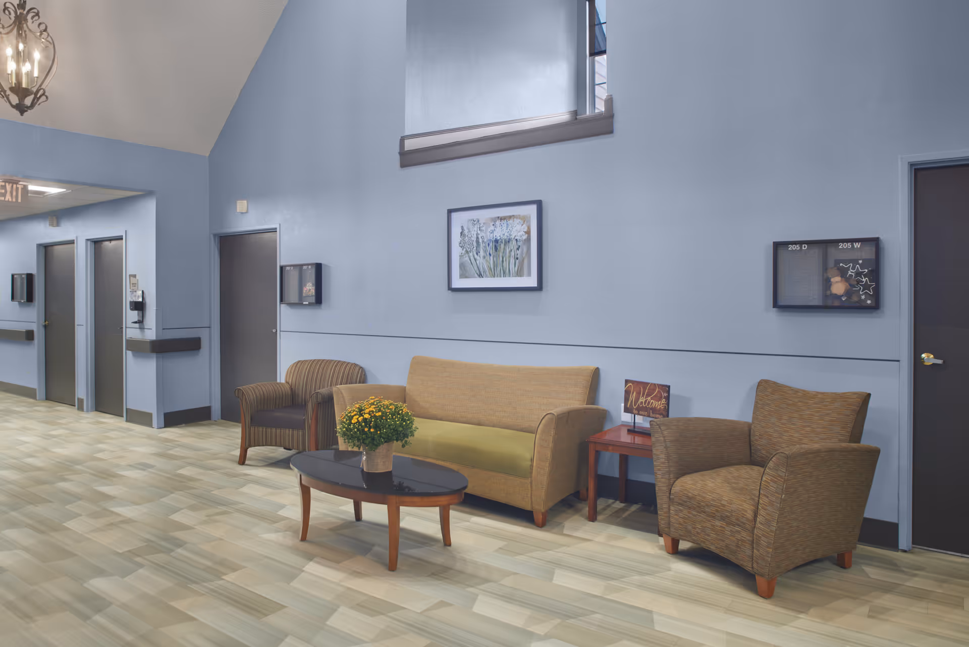 A senior living facility seating area with a sofa, armchairs, coffee table and hallway doors along a blue wall.