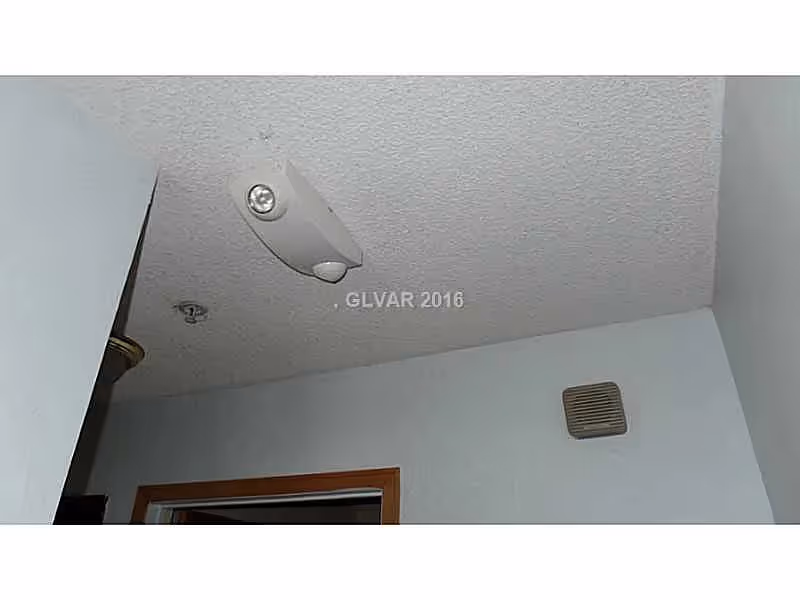 Ceiling and upper wall of an interior room showing a ceiling light or sensor, an air vent, and a doorway trim.