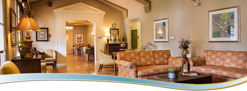 Comfortable communal living room/lounge with patterned sofas, armchairs, a coffee table and a view into a dining area.