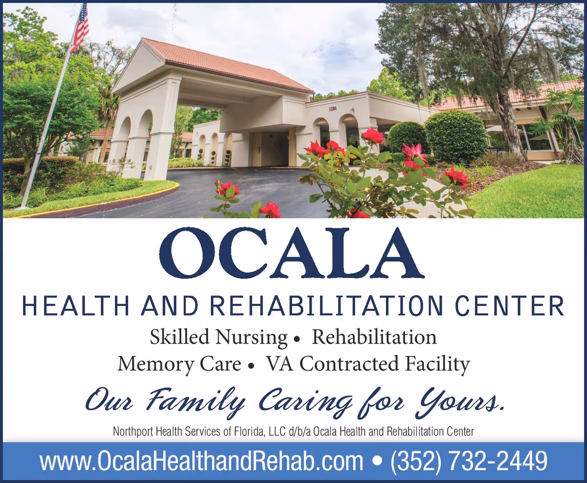 Exterior view of Ocala Health and Rehabilitation Center showing the entrance with a covered driveway, surrounded by greenery and red flowers, with an American flag on the left side.