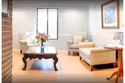 Bright living room with cream seating, a wooden coffee table, flowers, and a window.
