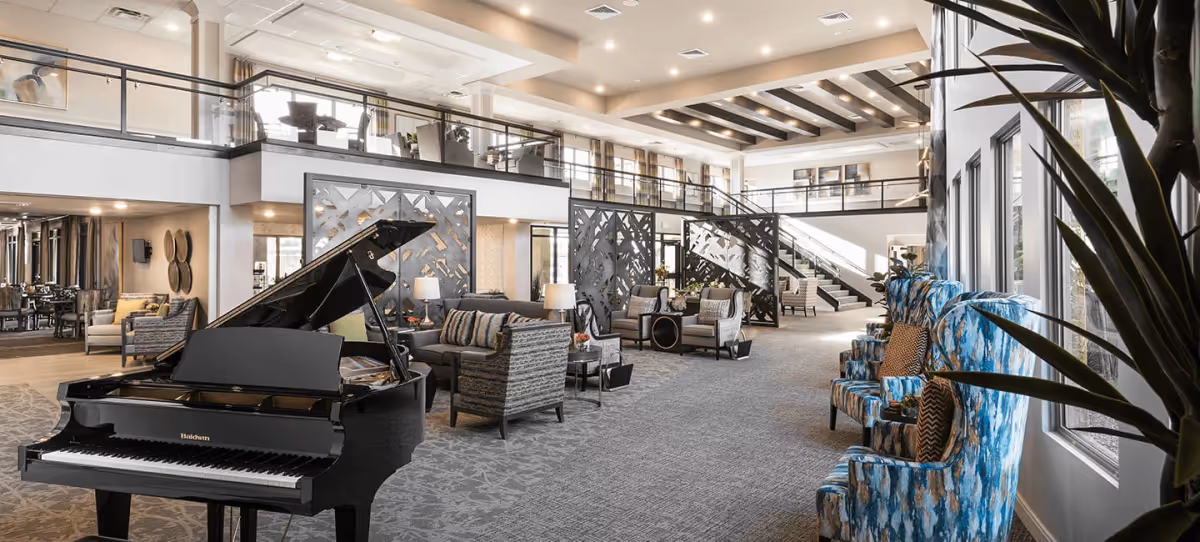 Spacious two-story communal lounge with a grand piano, multiple seating areas, decorative partitions, and large windows.