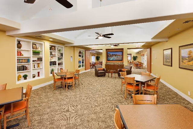 Large communal dining and lounge area with multiple tables and chairs, built-in bookshelves, and a seating area with a TV.