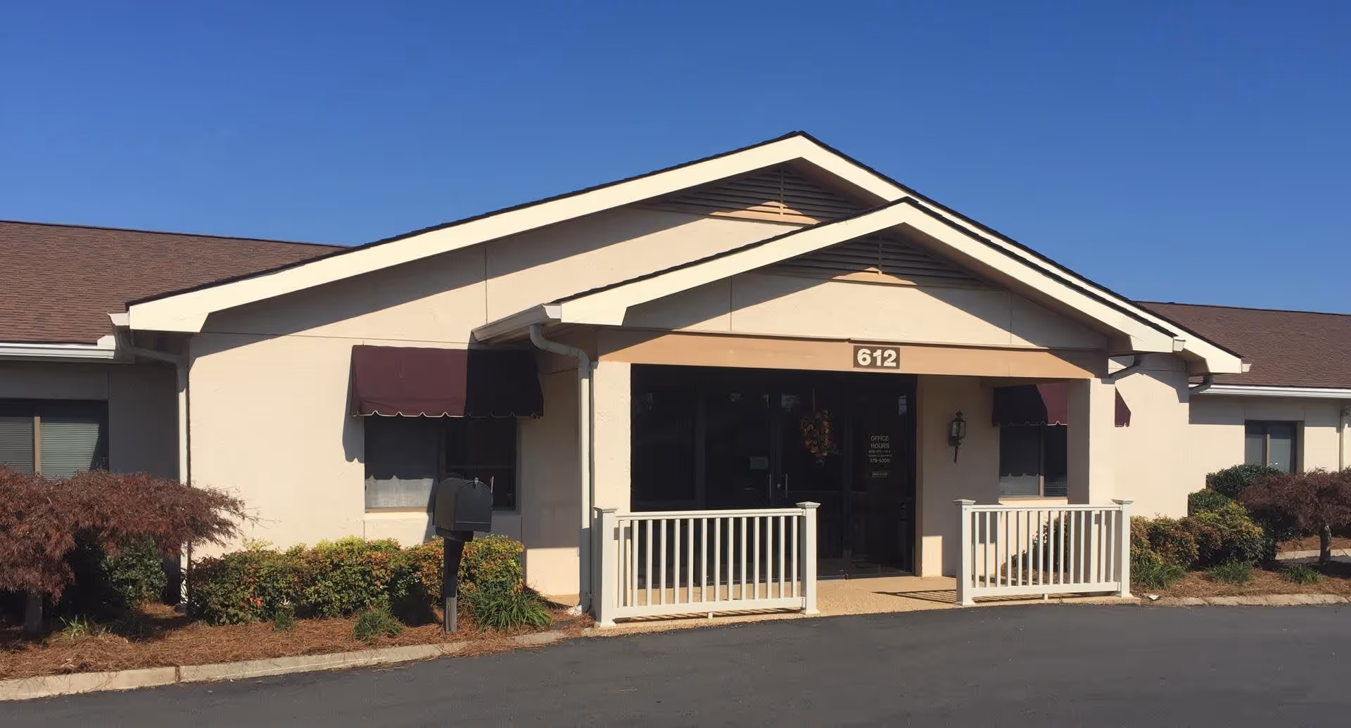 Front entrance of a single-story senior living building with a covered porch, white railings, awnings, and the address number 612 above the door.