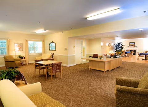 Bright common room with sofas, armchairs, small dining tables, and a reception desk opening into a dining area.