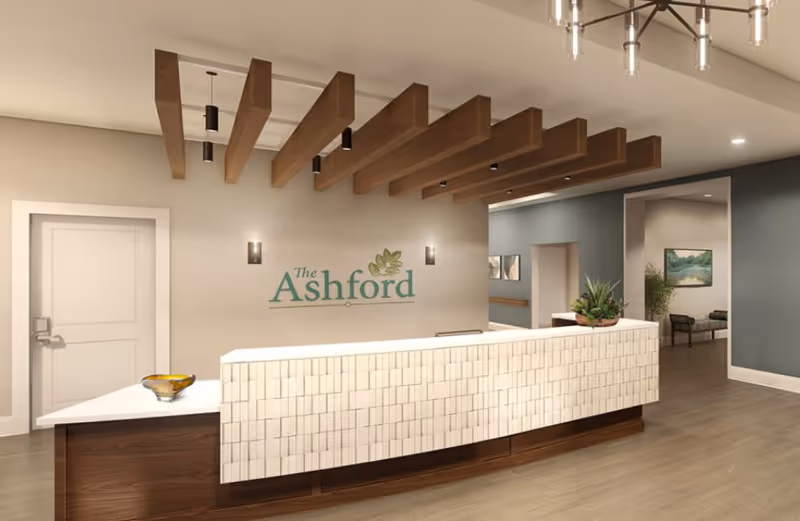 A reception desk and lobby area with a sign reading 'The Ashford,' wood ceiling beams, and seating visible in the background.