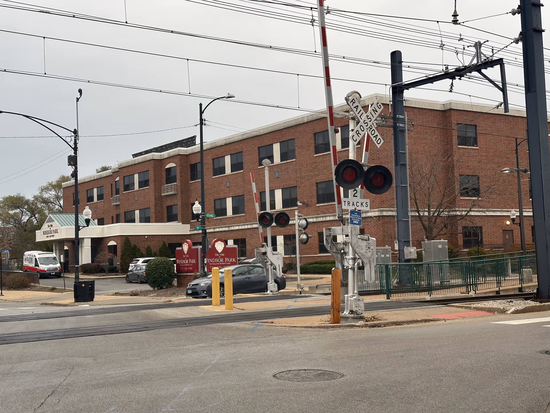 Three-story brick senior living building labeled Windsor Park beside a street-level railroad crossing with signals and gates in front.
