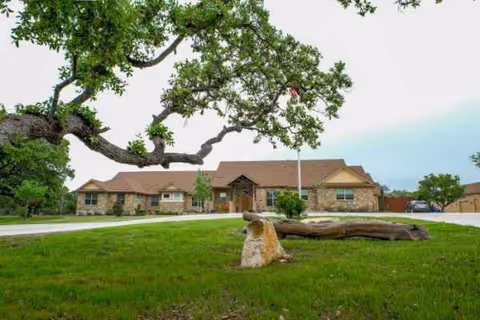 Exterior view of Tiffin House senior living facility's front, brick facade, green lawn, and trees.