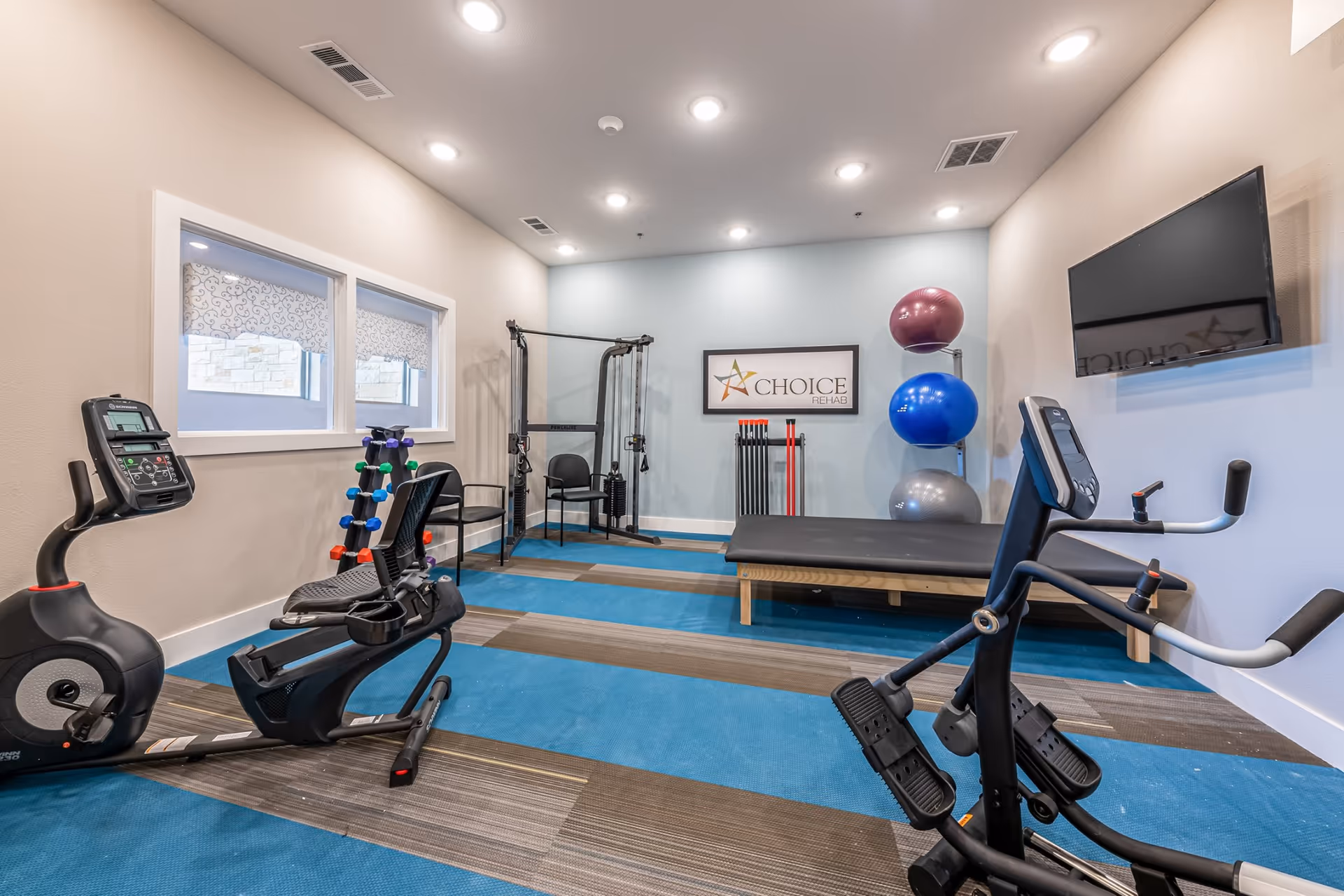 Interior gym at Buda Oaks with exercise bike, weights, and a treatment bench.