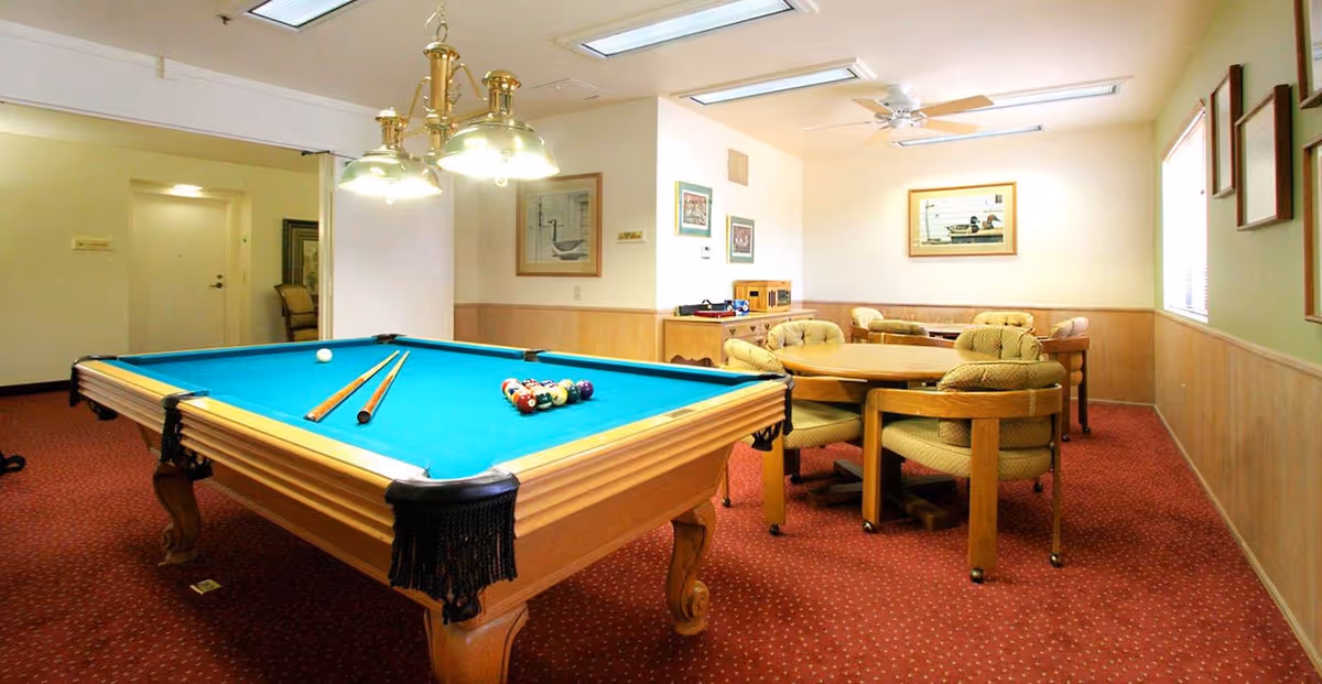 Recreation room with a pool table, cue sticks and balls, and a round table surrounded by padded chairs.