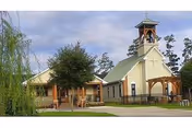 Exterior view of a light-colored church-style building with a bell tower and covered entryway on landscaped grounds.