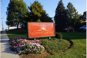Red entrance sign reading 'TOWNE CENTRE' on a landscaped lawn with flowers, shrubs, parked cars and tall trees in the background.