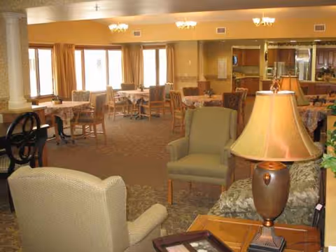 Senior living lounge with comfortable seating, tables, lamps, and large windows.