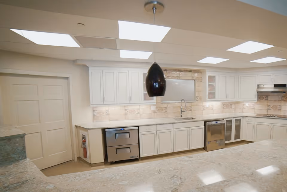 Bright modern kitchen with white cabinets, marble countertops, stainless appliances and a central pendant light.