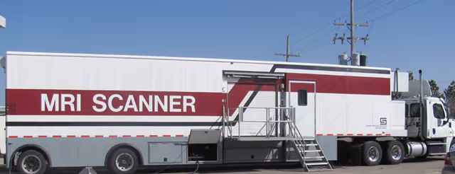 A white and maroon mobile MRI scanner trailer parked outdoors with a set of stairs leading to its entrance.