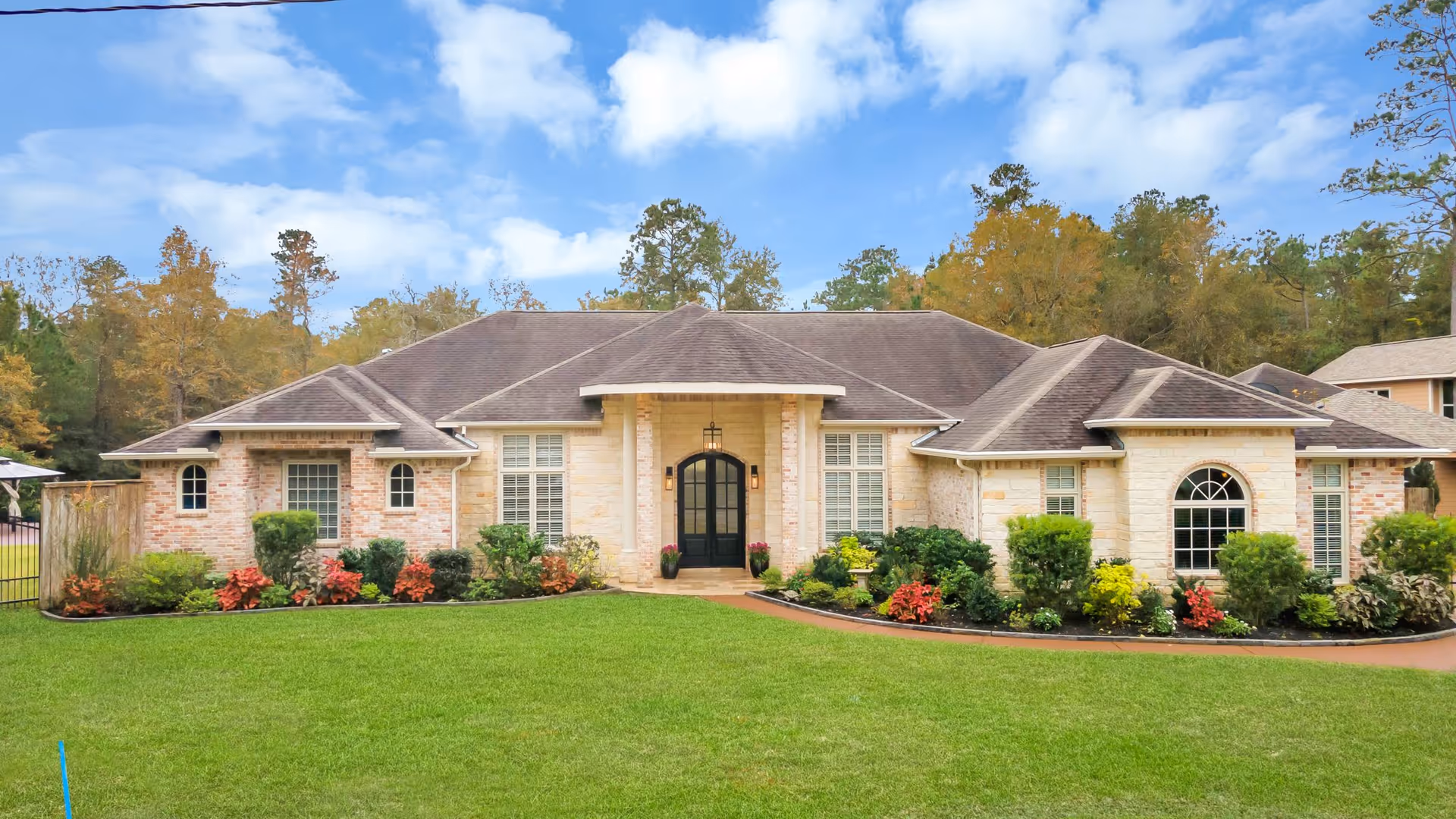 Single-story brick and stone home with a manicured lawn and landscaped front yard under a blue sky.