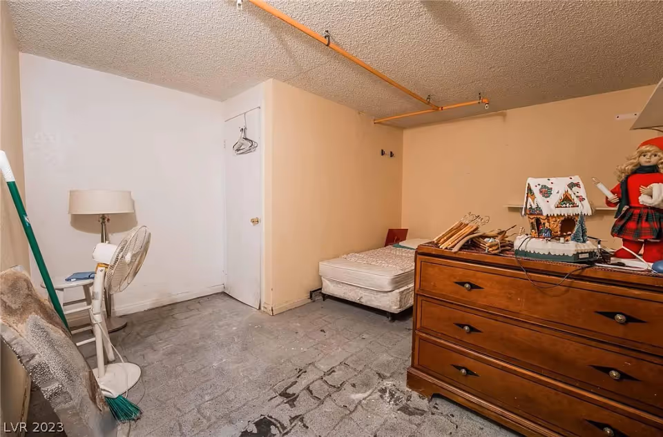 Small sparsely furnished bedroom with a mattress on the floor, a wooden dresser with holiday decorations and a standing fan.