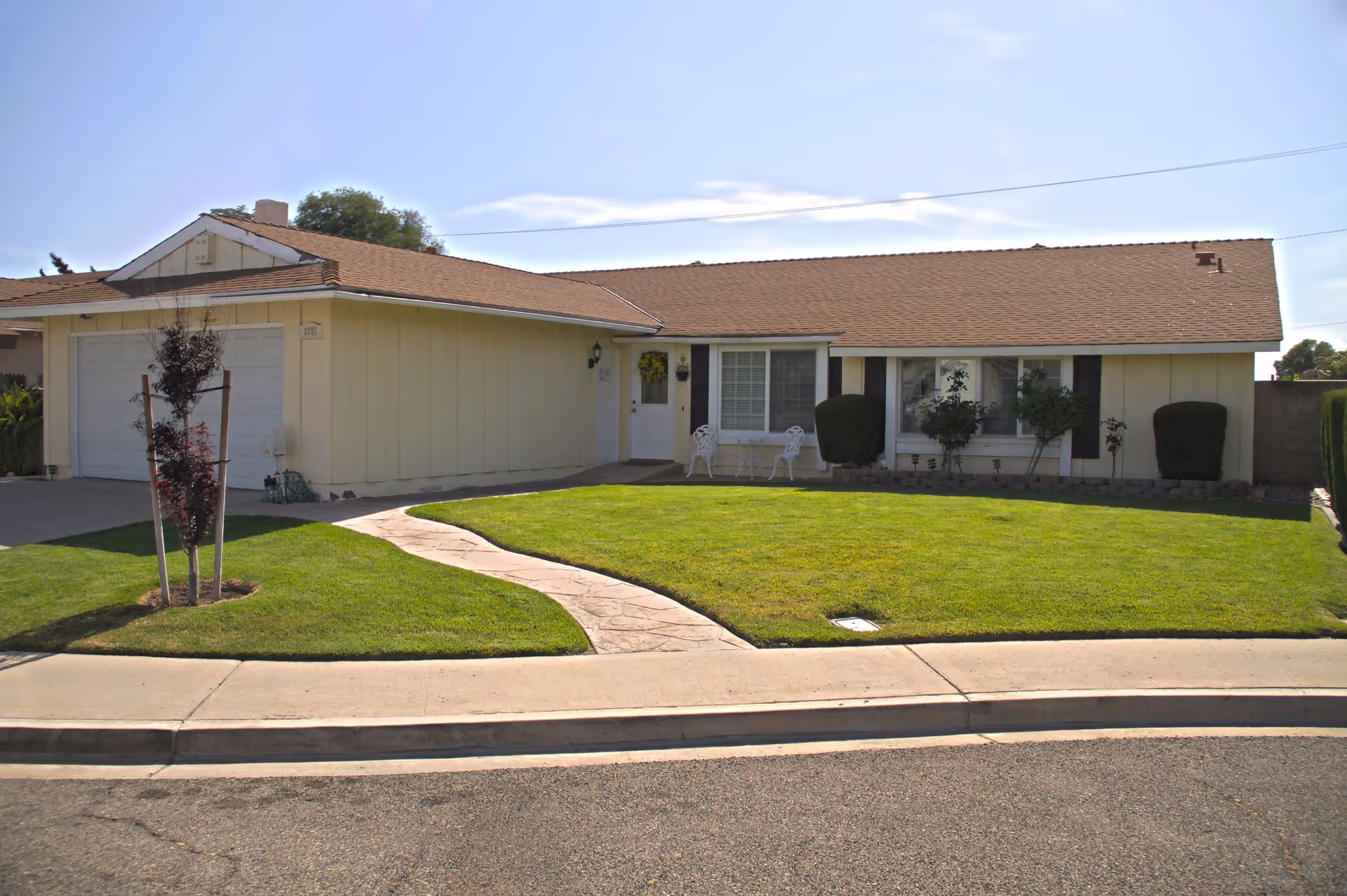 Single-story ranch-style home with a manicured front lawn, curved stone walkway, and attached two-car garage.