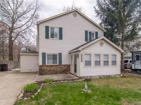 Two-story beige building with green shutters and a small front extension, seen with driveway and lawn.