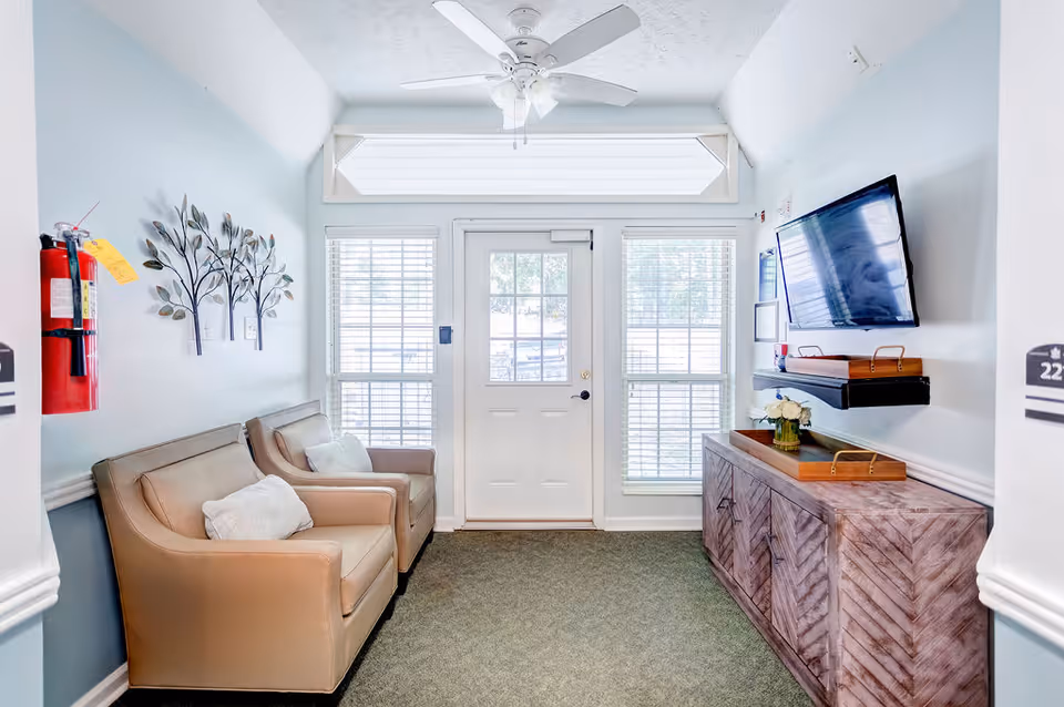 Bright entry lounge with two armchairs, a wall-mounted TV above a wooden console, and a door with sidelights.