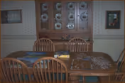 Dining room with a wooden table and chairs, a china cabinet displaying plates, framed pictures on the walls, and a partially completed jigsaw puzzle on the table.