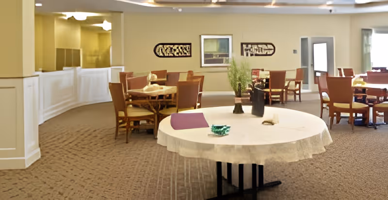 Carpeted communal dining area with round tables and chairs and a centerpiece on a table.