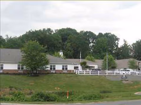 A single-story senior living facility with a white fence, green lawn, and trees.