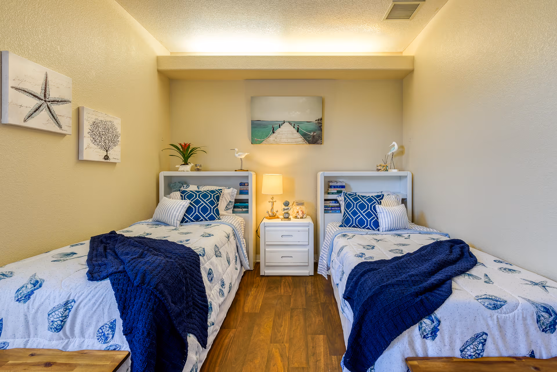 Coastal-themed bedroom with two twin beds, a central nightstand and wall artwork above.