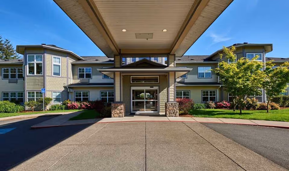 Front exterior view of Middlefield Oaks Assisted Living and Memory Care building with a covered entrance, landscaped greenery, and clear blue sky.