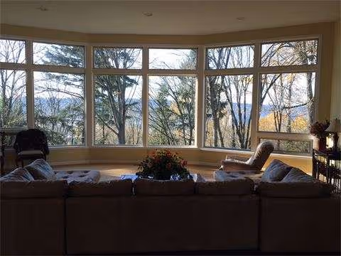A sunlit living room with a curved wall of windows and a beige sectional sofa.