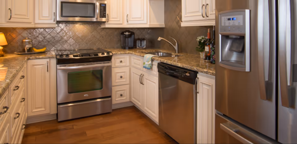 Well-lit modern kitchen with stainless steel appliances, granite countertops, white cabinets, and hardwood floors.