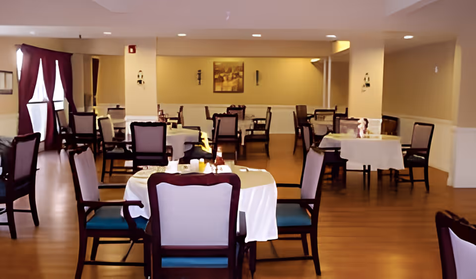 Interior dining room with multiple set tables and chairs and wood flooring in a senior living facility.