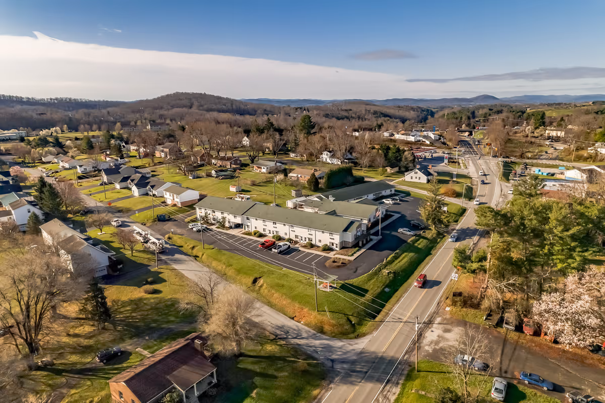 Aerial view of a residential area featuring a large building with a parking lot, surrounded by houses, trees, and roads under a clear blue sky.