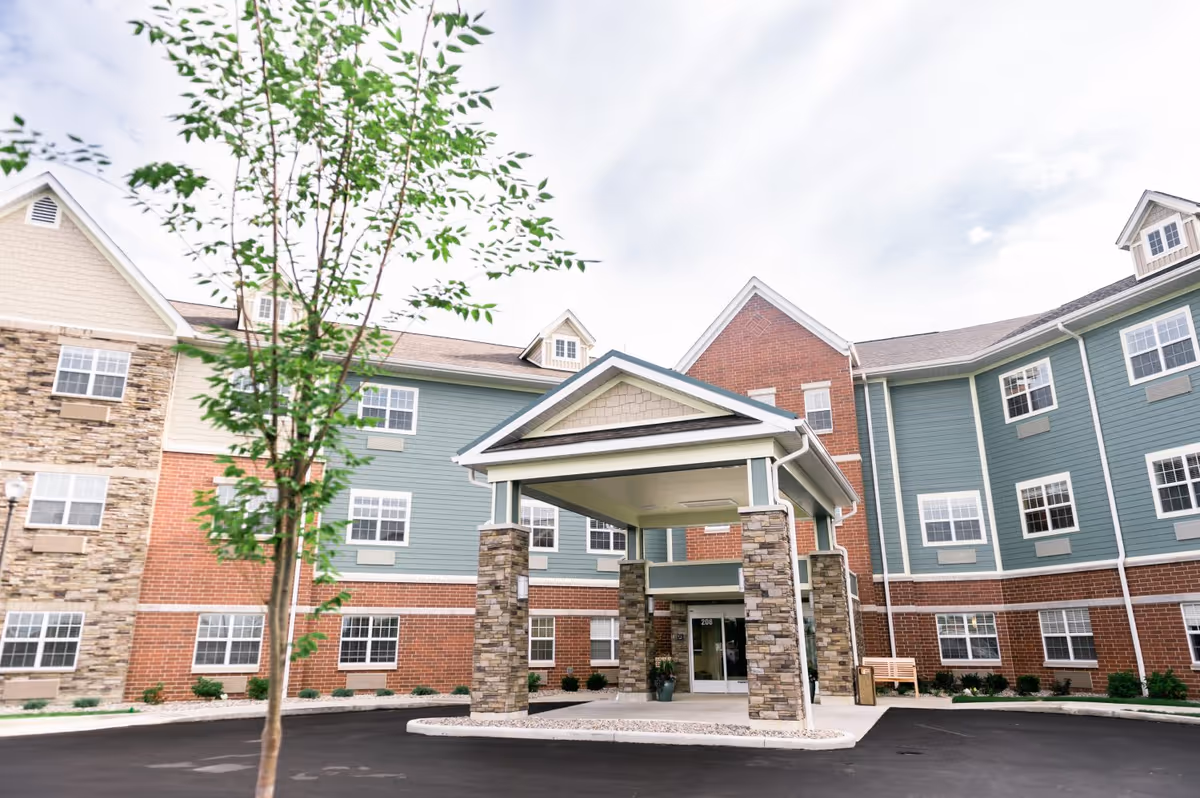 Front entrance of a multi-story senior living building with a covered porte-cochere and brick and siding facade.