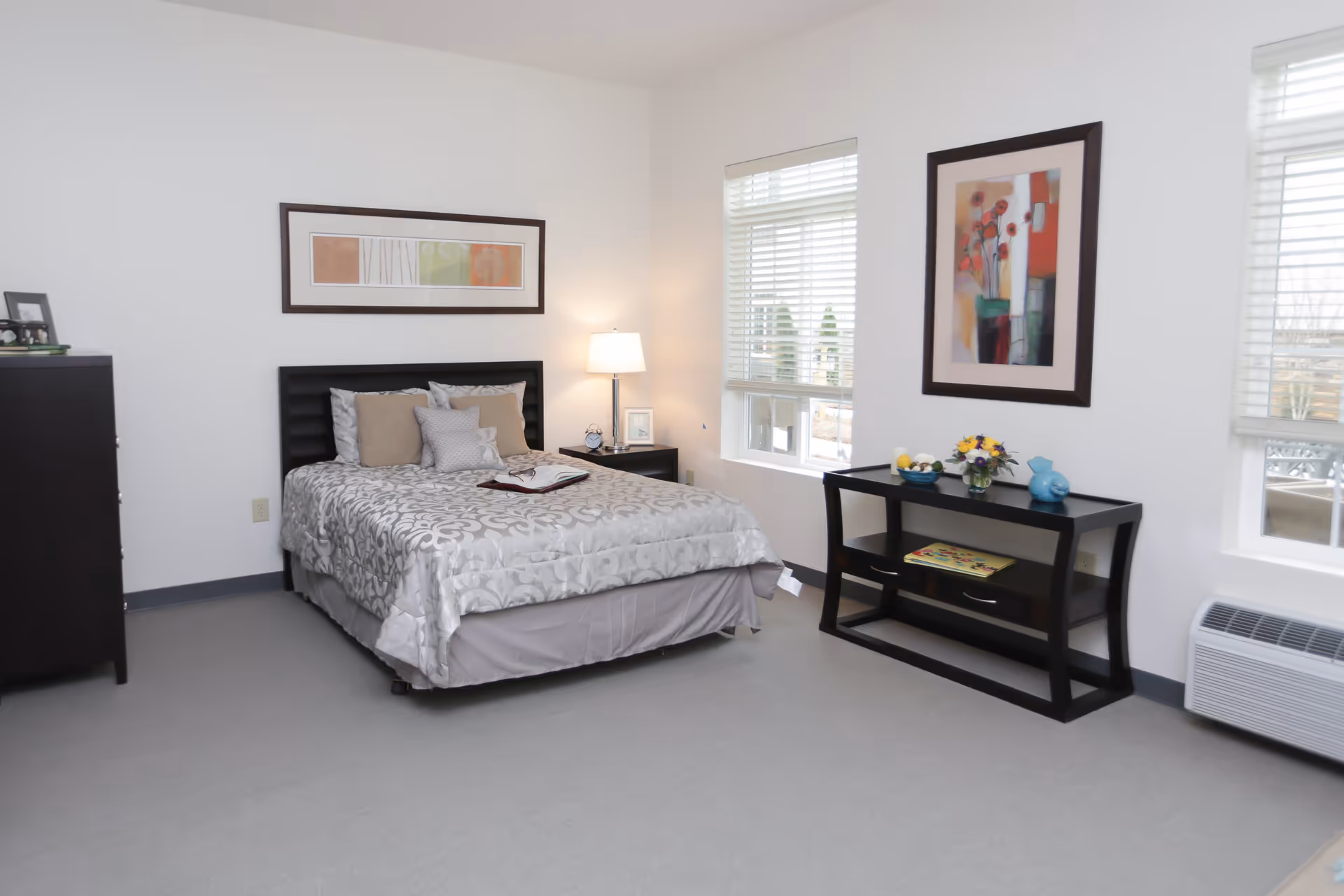 Bright, tastefully decorated bedroom with a bed, nightstand, dresser and a console table beneath framed artwork.
