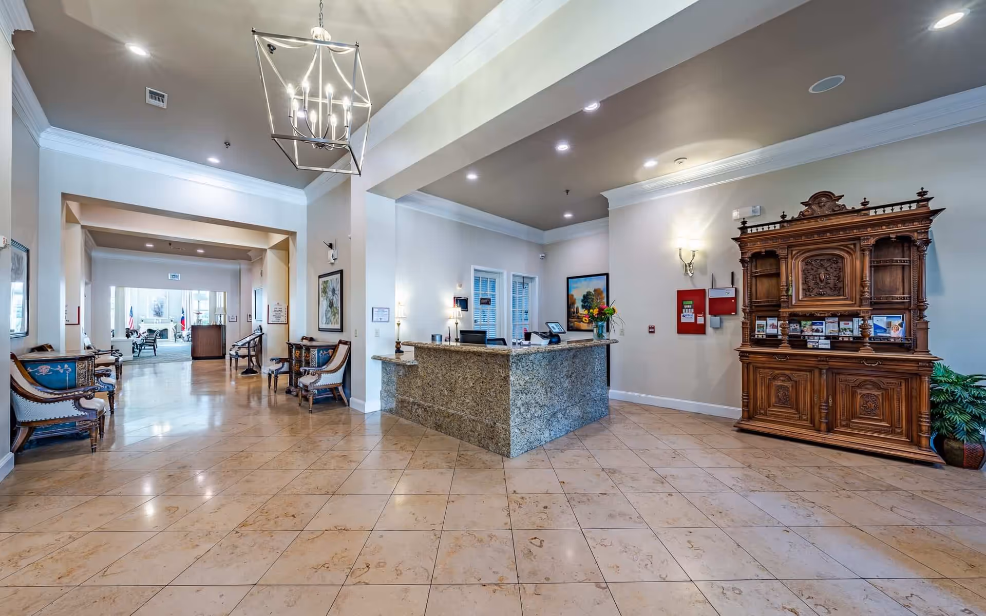 Spacious senior living reception lobby with a granite front desk, seating areas, and an ornate wooden cabinet.