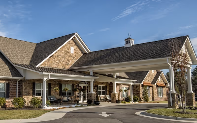 Entrance of a brick-and-stone senior living facility with a covered porte-cochère and landscaped driveway.