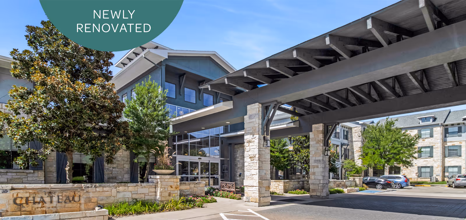 Exterior view of Chateau McKinney senior living facility showing a newly renovated entrance with stone pillars, a covered driveway, landscaped greenery, and a clear blue sky.