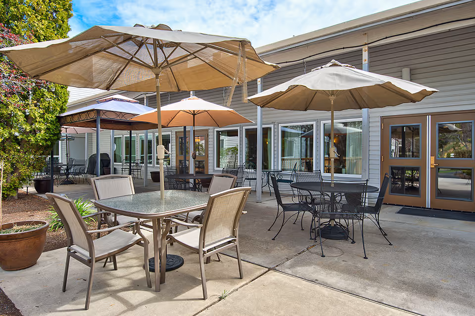 Outdoor patio with tables, chairs, and large umbrellas outside a retirement community building.