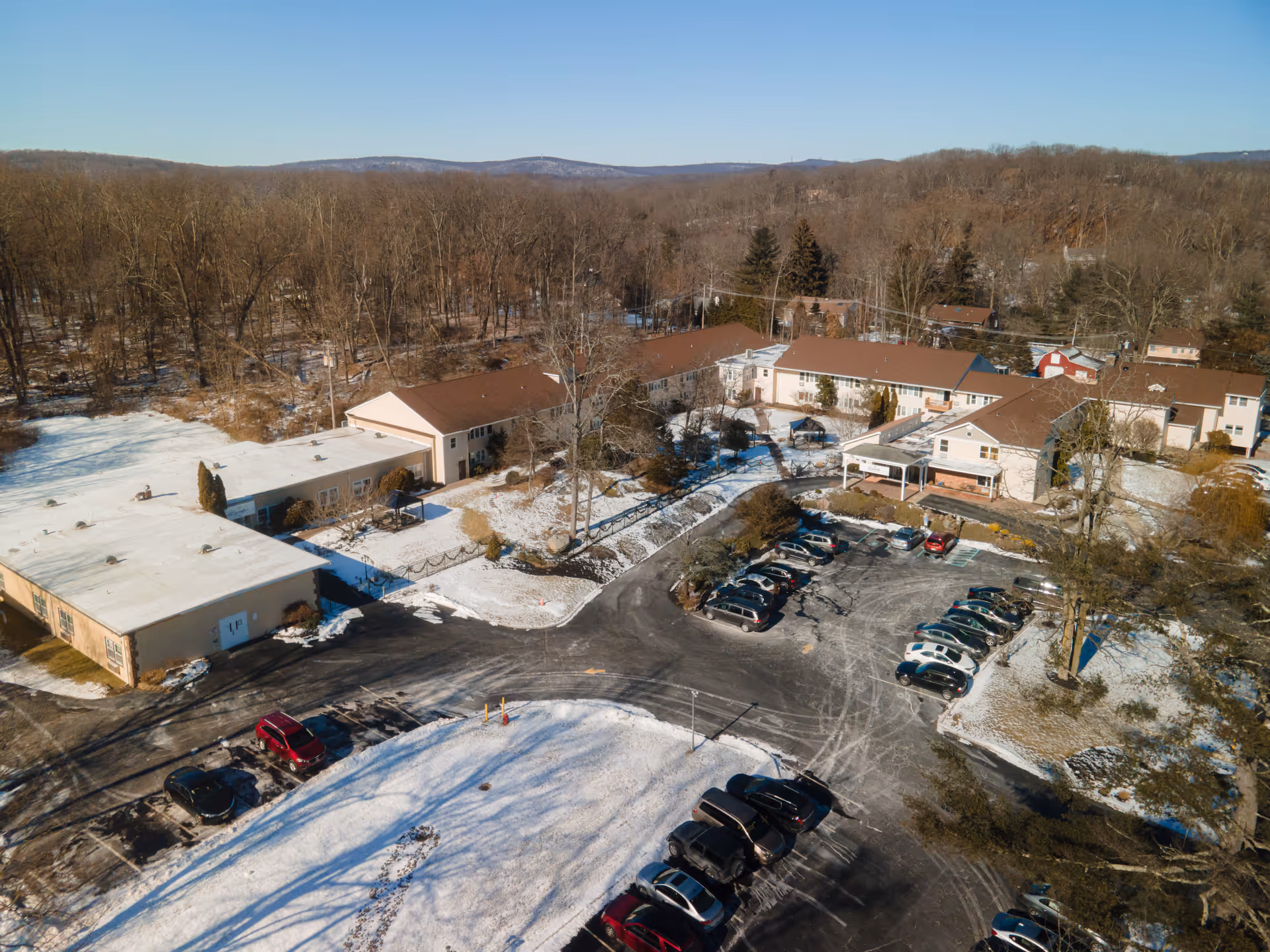Aerial view of a nursing home complex with multiple low-rise buildings, a snowy landscape, and a parking lot with cars.
